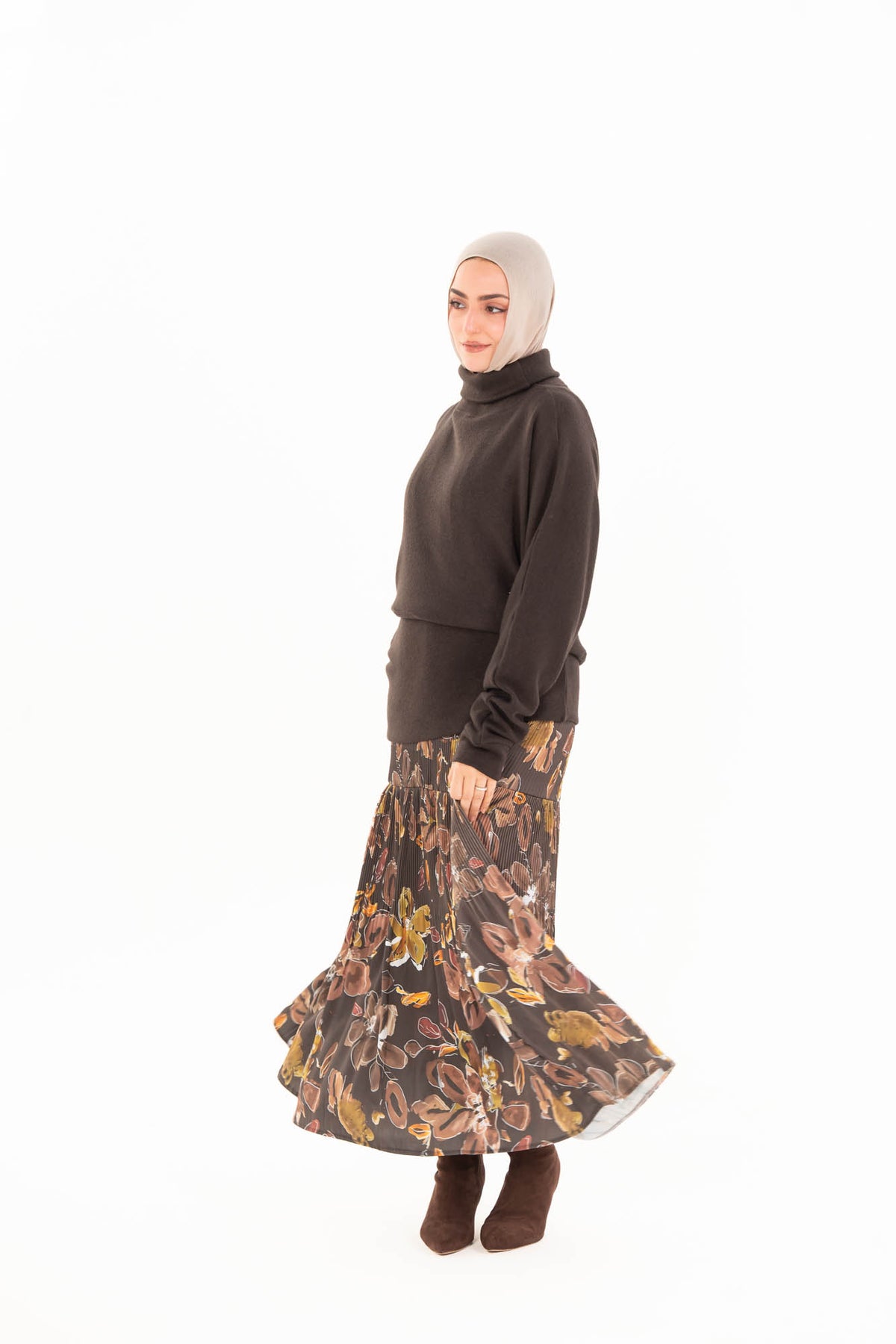 Full length model wearing a brown high-neck top, printed pleated maxi skirt and brown boots.